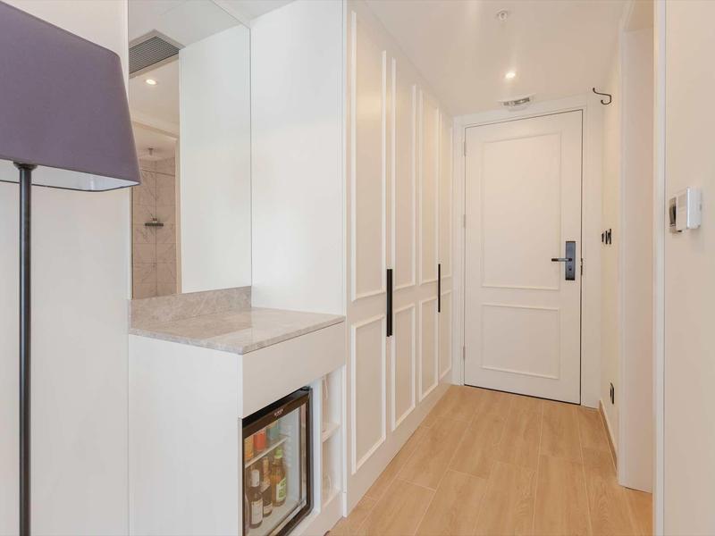 Heller Flur mit Holzboden, weißer Tür, Einbauschrank und kleinem Kühlschrank rechts.