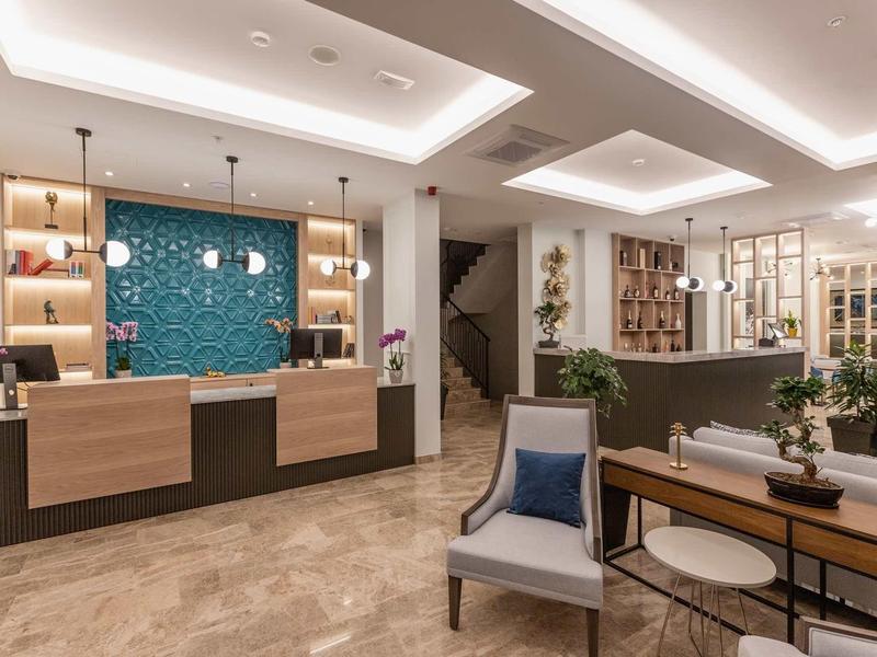 Moderner Empfangsbereich mit Tresen, Sitzbereich, Regalen und stilvoller Beleuchtung in warmen Tönen.