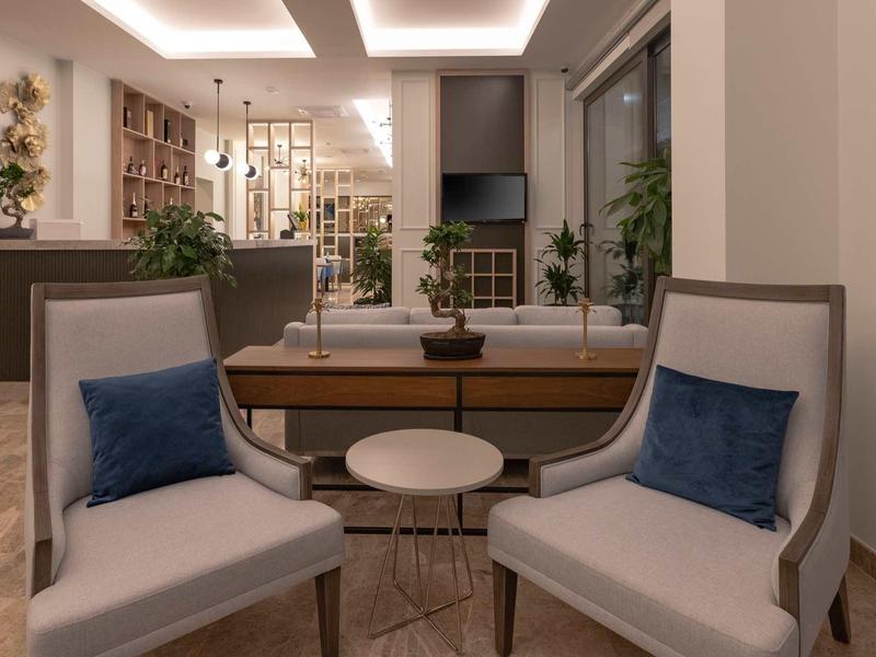 Moderner Wohnraum mit zwei beigen Sesseln, blauen Kissen, Holztisch und offener Küche im Hintergrund.