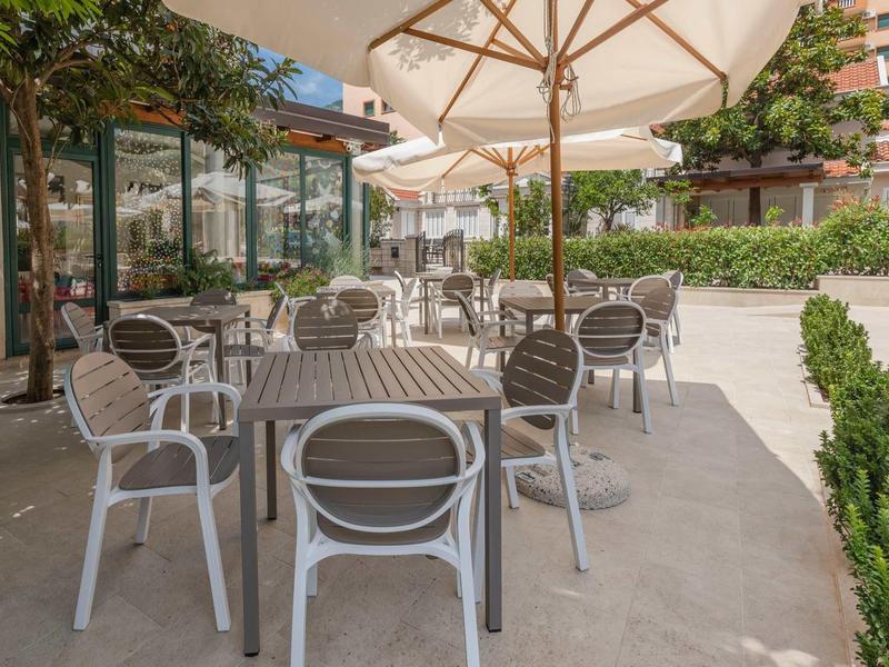 Freiluftterrasse mit Tischen, Stühlen und großen Sonnenschirmen neben einem Gebäude.