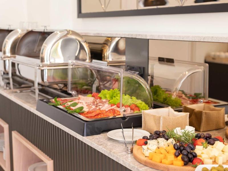 Buffet mit verschiedenen warmen Speisen und frischem Obst auf einem langen Tisch in modernem Raum.