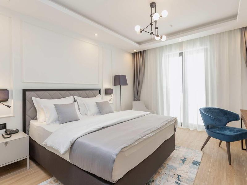 Modernes Schlafzimmer mit großem Bett, weißen Wänden, grauer Bettdecke und blauen Sesseln.