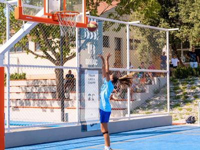 Kind gooit basketbal in de ring op een zonnig buitenveld.