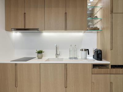 Moderne Küchenzeile im Hotelzimmer mit Holzfronten, Kochfeld, Spüle und Kaffeemaschine.