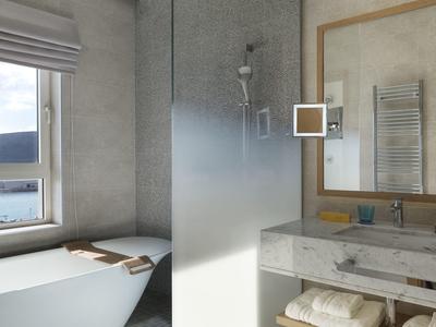 Modernes Bad mit freistehender Badewanne, großem Fenster und grauer Steinwand im Hotelzimmer.