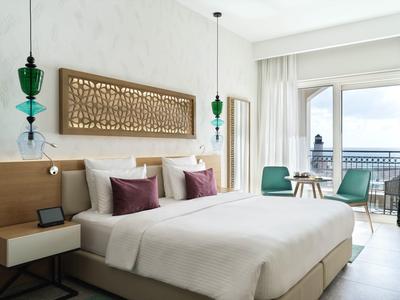 Modernes Hotelzimmer mit Doppelbett, Balkon und Blick auf Wasser bei Tageslicht.