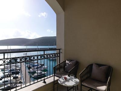 Balkon mit Stühlen und Tisch, Blick auf Yachthafen und Hügel bei klarem Wetter.