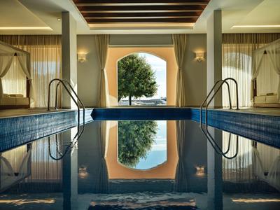 Innenpool mit ruhigem Wasser, breiten Treppen und Blick auf Baum und Meer durch ein großes Fenster.