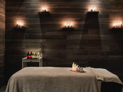Dunkler Wellnessraum mit Massagebank, Kerzen und Tablett mit ätherischen Ölen.