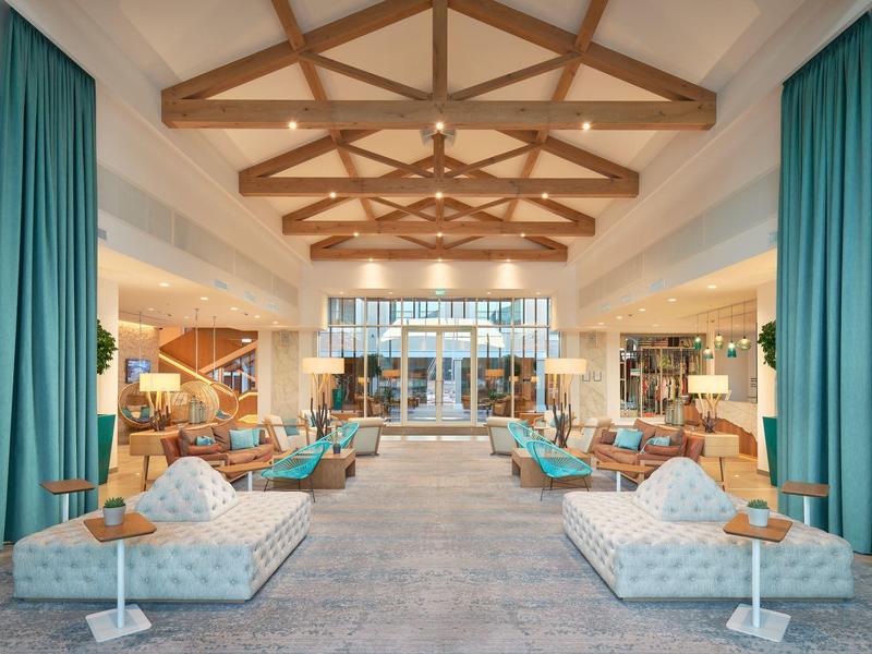 Ruime hotel lobby met houten balkenplafond, blauwe gordijnen en moderne zitgedeeltes.