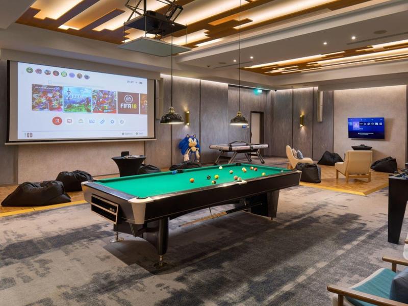 Moderne gemeenschappelijke ruimte met pooltafel, zitzakken en groot scherm in een hotel.