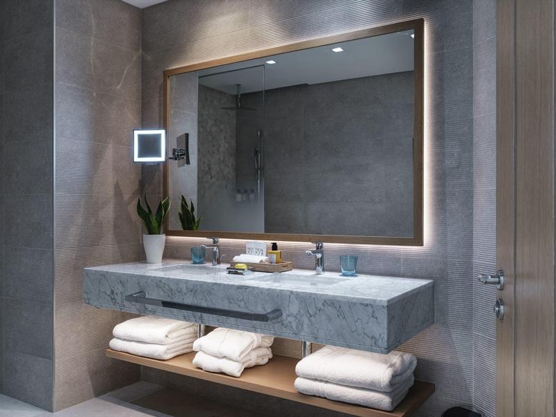 Moderne badkamer met verlichte spiegel, dubbele wastafel en grijze muren.