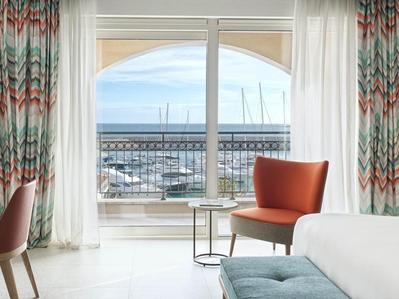 Moderne hotelkamer balkon met uitzicht op jachthaven en zee onder een blauwe lucht.