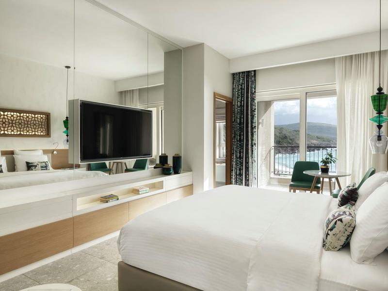 Modern hotelkamer met groot bed, flatscreen-tv en uitzicht op bergen door raam.