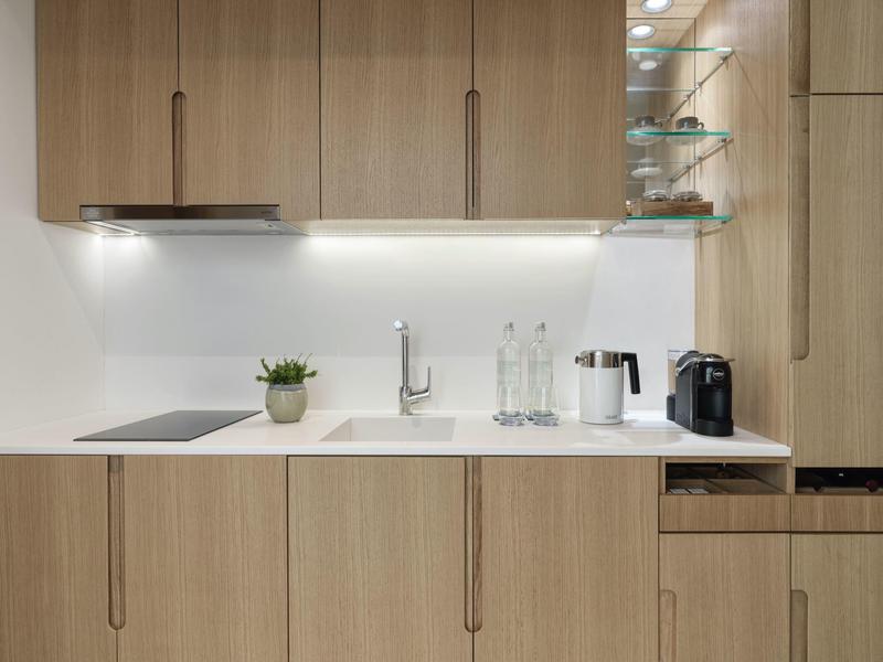 Moderne kitchenette met houten kasten, wit aanrecht en kleine apparaten.