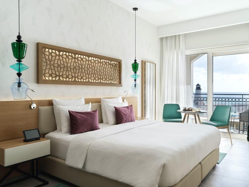 Modern hotelkamer met tweepersoonsbed, houten meubels, balkon en zeezicht.