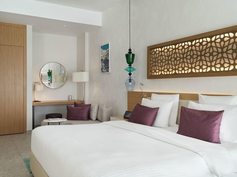 Modern hotelkamer met een groot bed, paarse kussens en decoratieve wandlamp.