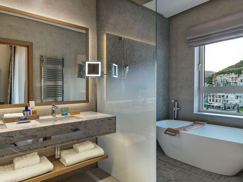 Moderne badkamer met vrijstaand bad, grote spiegel en handdoeken onder de wastafel.