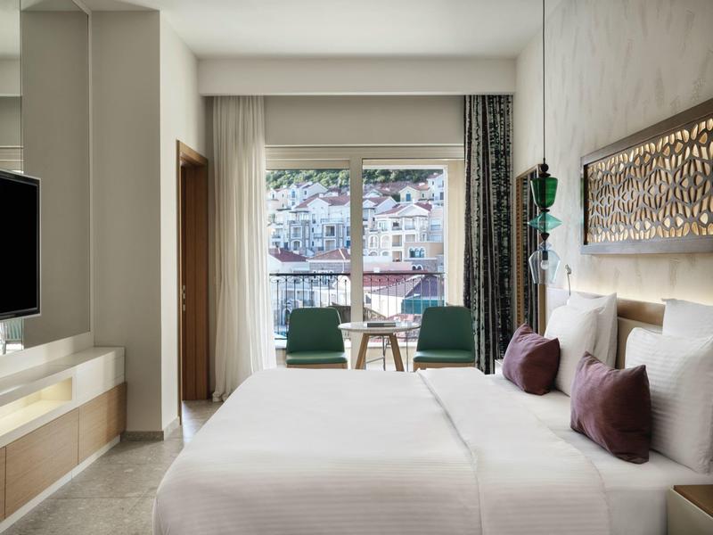 Moderne hotelkamer met tweepersoonsbed, zithoek en balkon met uitzicht op de stad.