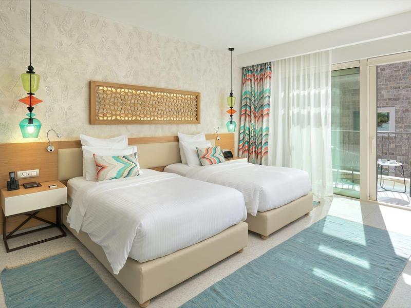 Modern hotelkamer met twee eenpersoonsbedden, lichte inrichting en balkon met uitzicht naar buiten.