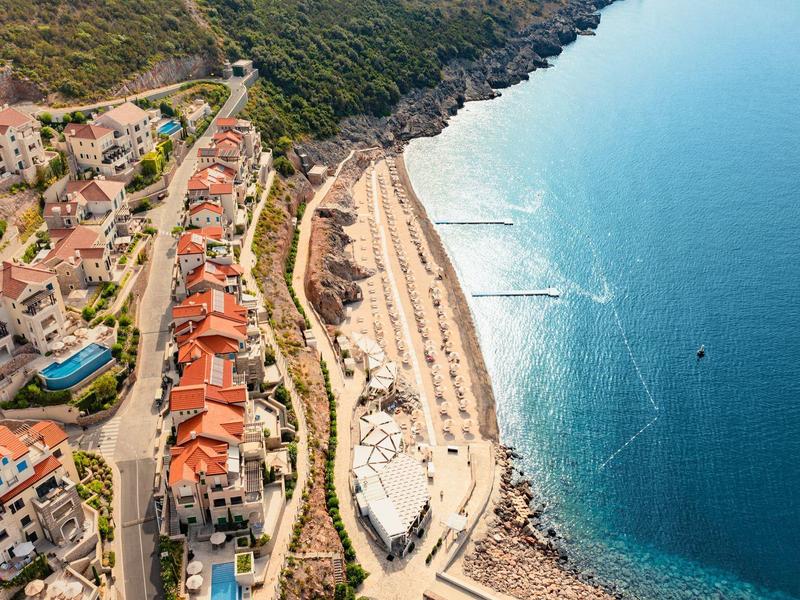 Luchtfoto van een strand met parasols naast een hotel in een kustplaats.