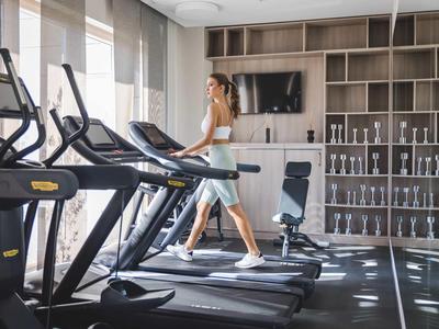 Kobieta trenująca na bieżni w jasnej, nowoczesnej siłowni hotelowej.