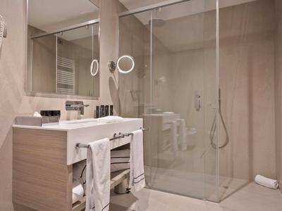 Modernes Badezimmer mit Glasdusche, großem Spiegel, Waschbecken und Handtüchern in hellem Design.