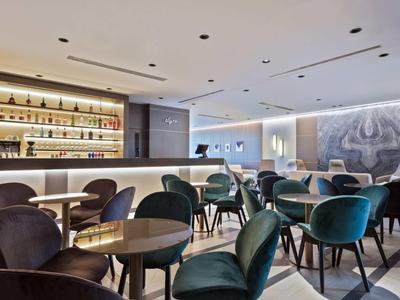 Nowoczesny bar hotelowy z okrągłymi stołami, wygodnymi krzesłami i podświetlanym kontuarem.