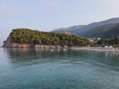 Küstenlinie mit bewaldetem Kap, klarem ruhigem Wasser und Strand vor bewaldeten Hügeln.