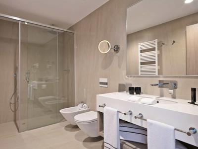 Modernes Badezimmer mit großer Dusche, Bidet, Waschbecken, Spiegel und Handtuchhalter in Beige-Tönen.