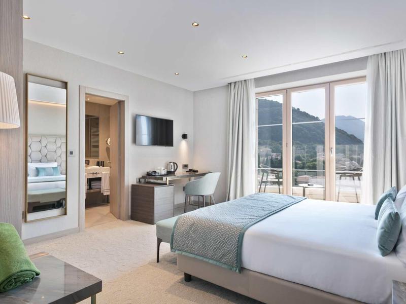 Helles Hotelzimmer mit großem Bett, moderner Einrichtung und Balkon mit Bergblick.