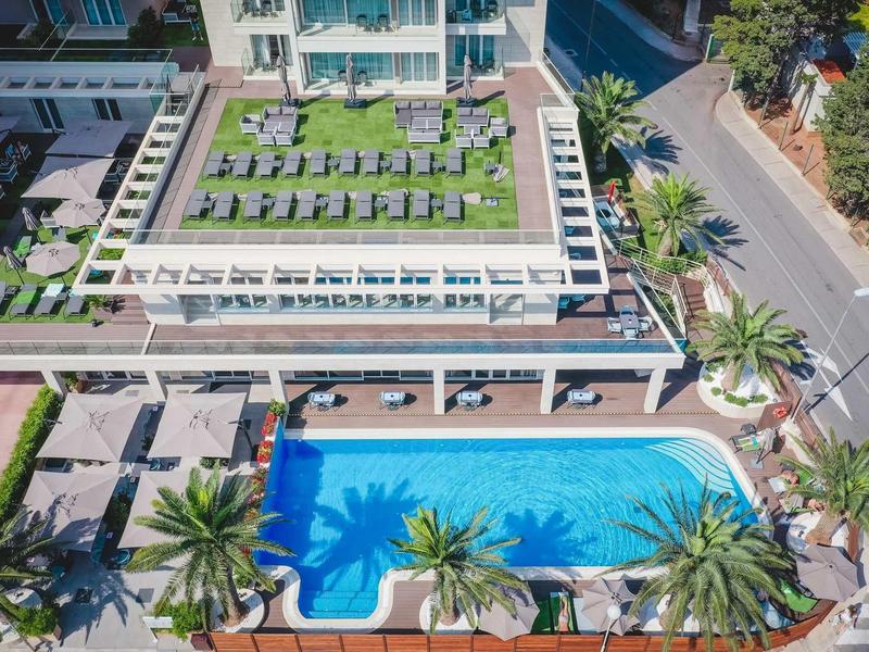 Poolanlage mit blauer Wasserfläche, Liegen und grüner Dachterrasse in modernem Wohnkomplex.