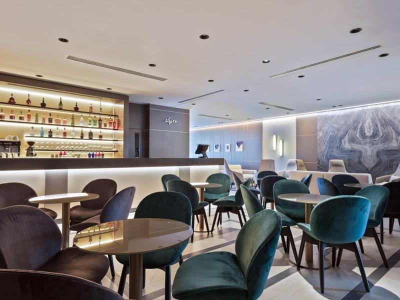 Moderner Barraum mit runden Tischen, samtigen Stühlen und beleuchtetem Regal mit Flaschen.