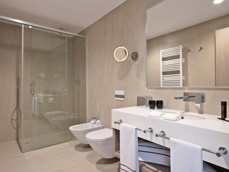 Modernes Badezimmer mit großer Dusche, Bidet, Waschbecken, Spiegel und Handtuchhalter in Beige-Tönen.