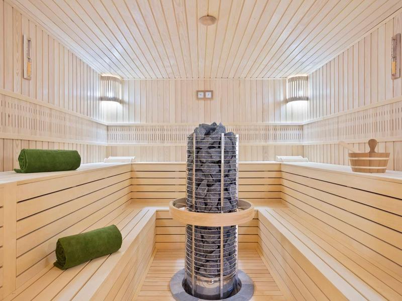 Helle Holzbänke und Wände in Sauna mit zentralem Steinkamin und grünen Handtüchern.