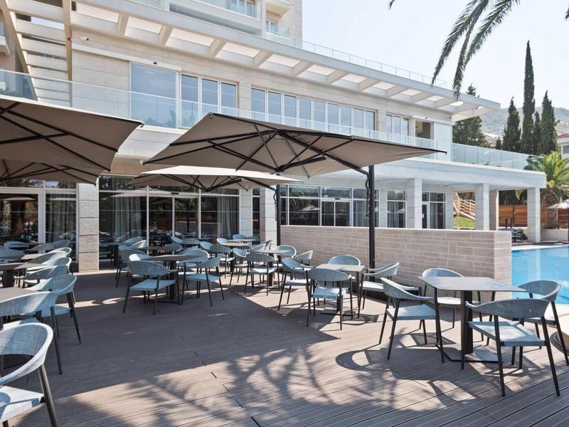 Freiluftterrasse mit Tischen, Stühlen und Sonnenschirmen neben einem blauen Schwimmbecken.