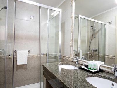 Helles Badezimmer mit Duschkabine, großem Spiegel und Doppelwaschbecken aus Granit.