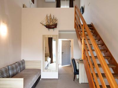 Wohnzimmer mit Holztreppe, kleinem Sofa, Schreibtisch und Wandspiegel mit Schiffsmodell.