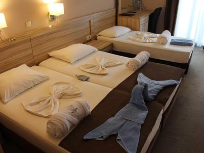 Drei Betten im Hotelzimmer, jeweils mit weißen Handtüchern kunstvoll gefaltet und brauner Tagesdecke.