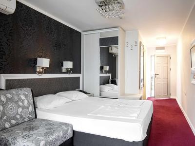 Modernes Hotelzimmer mit großem Bett, gemustertem Sessel, schwarzer Wand und rotem Teppichboden.