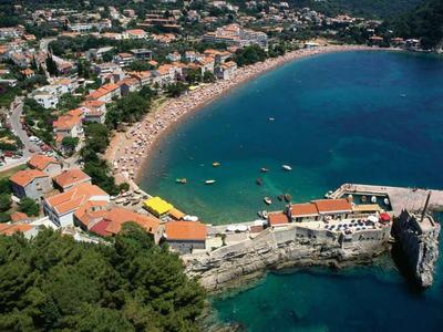 Küste mit kleinem Hafen, Stränden, dicht bebauter Siedlung und klarem blauem Wasser.