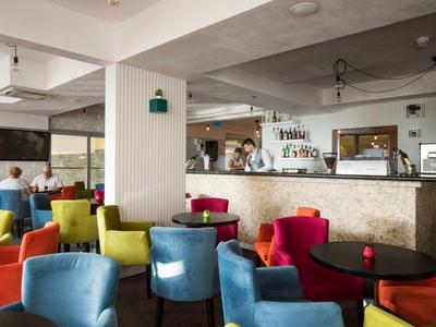 Kolorowe krzesła i stoły w nowoczesnym salonie hotelowym z barem w tle.