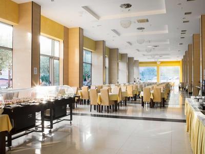 Jasna sala śniadaniowa w hotelu z stołami, krzesłami i bufetem.