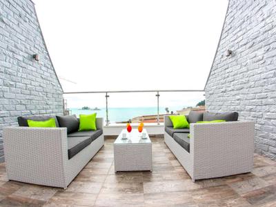 Nowoczesna przestrzeń na zewnątrz z białymi sofami, kolorowymi poduszkami i szklaną balustradą z widokiem na morze.