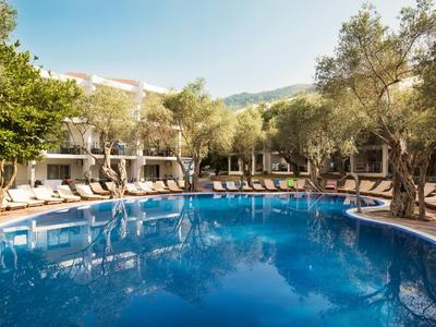 Okrągły basen na zewnątrz z leżakami i drzewami w ogrodzie hotelowym.