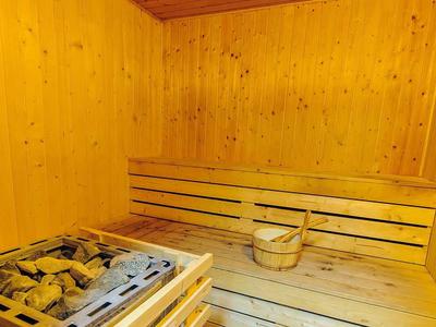 Holzsauna mit Holzbänken, Saunaofen mit Steinen und Holzeimer mit Schöpflöffel.