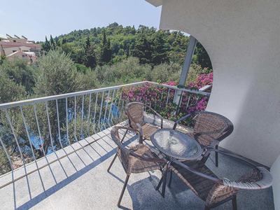 Balkon mit runden Tisch und vier Stühlen, umgeben von weißem Geländer und grüner Landschaft.