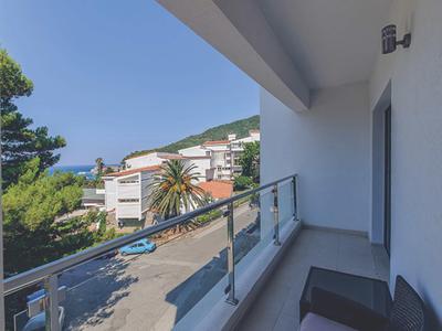 Balkon mit Glasgeländer, Blick auf Straße, Bäume und Wohnhäuser an sonnigem Tag.