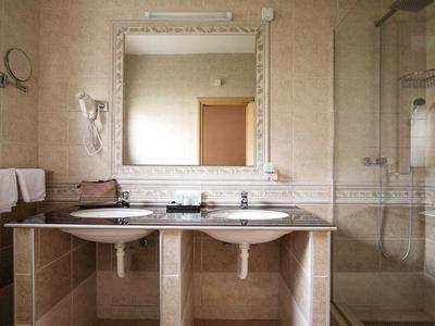 Badezimmer mit Doppelwaschbecken, großem Spiegel, Handtüchern, Fön und Duschecke mit Glastür.