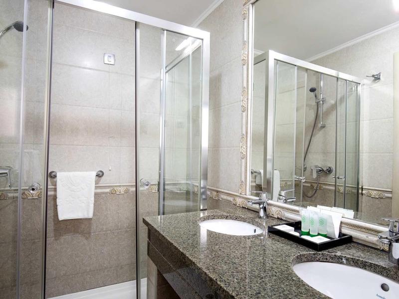 Helles Badezimmer mit Duschkabine, großem Spiegel und Doppelwaschbecken aus Granit.